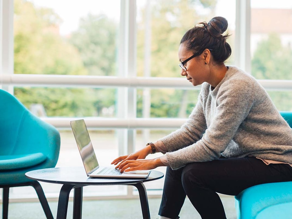 Dame sitter på en blå sofa og jobber på en laptop, til illustrasjon for sikker netthandel