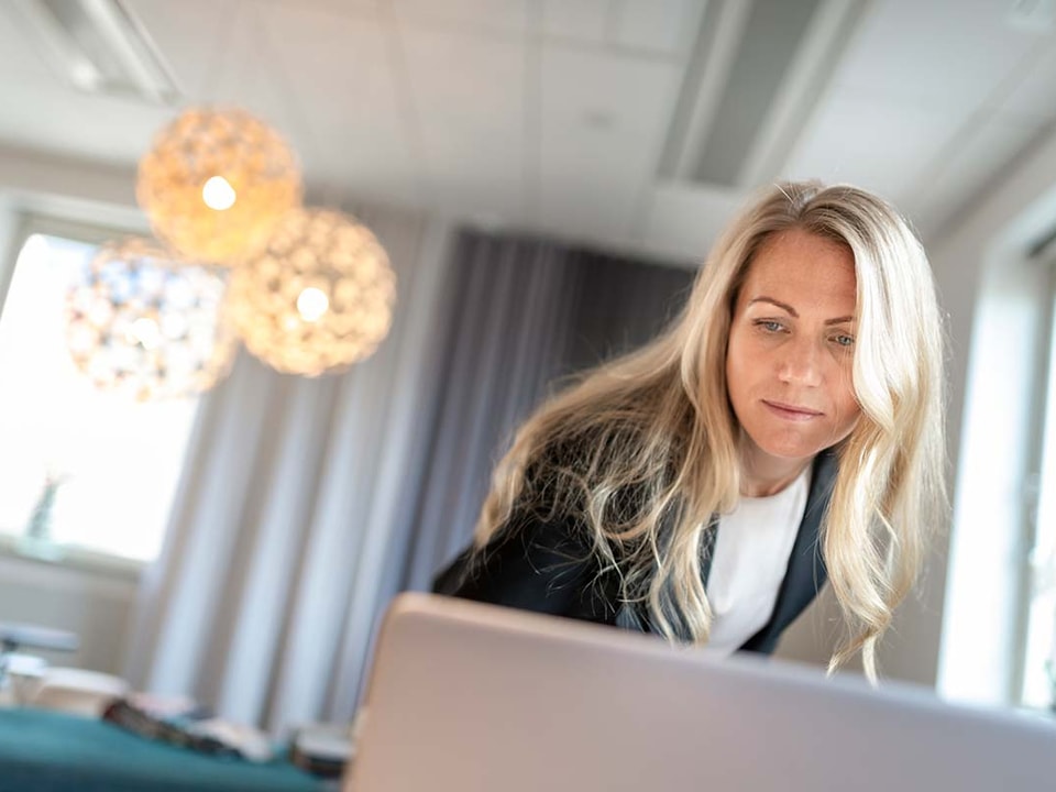 Kvinne med blazer lener seg over en datamaskin, til illustrasjon for finansavtaleloven